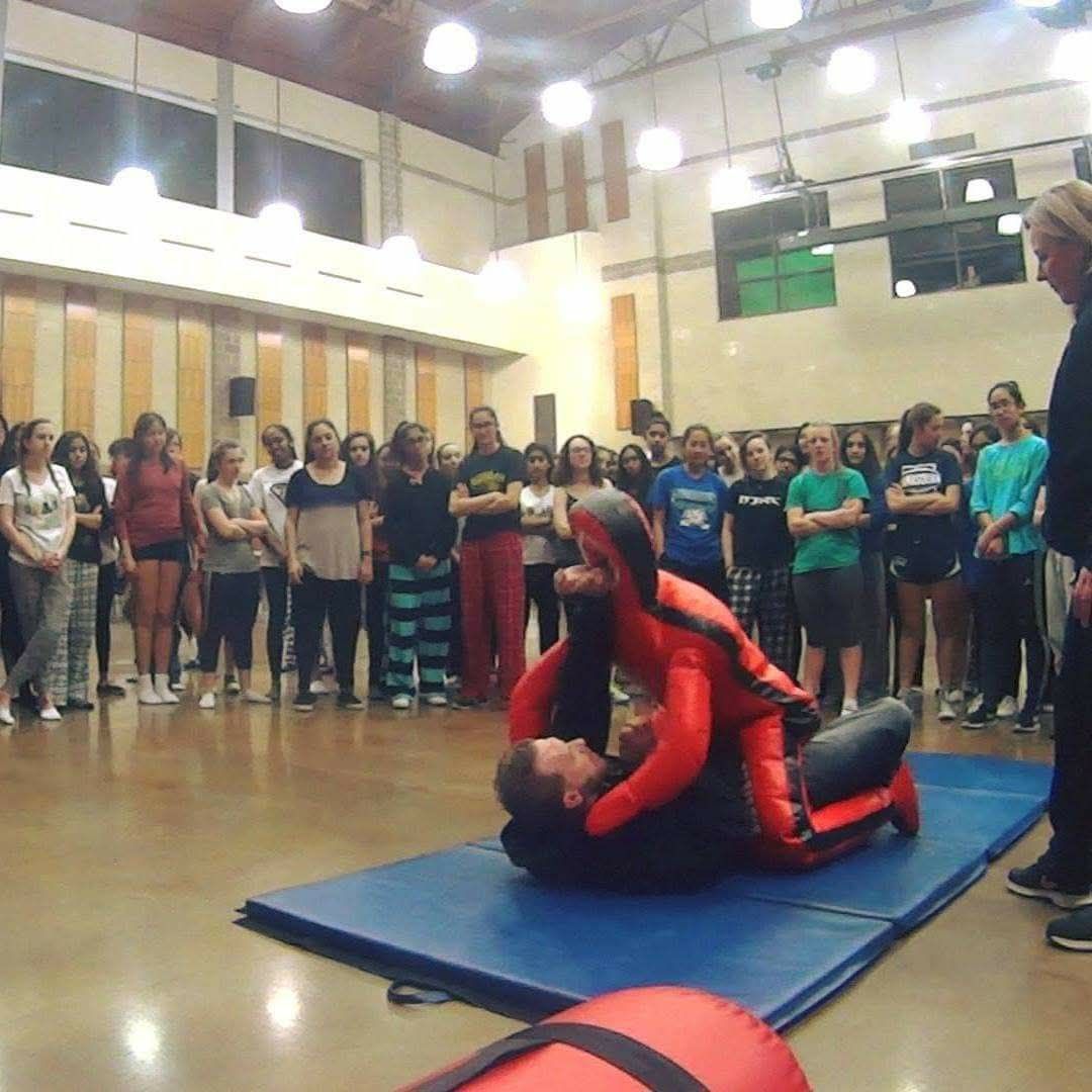M.A.C.S. self-defense training demonstration with a group gathered around the mat